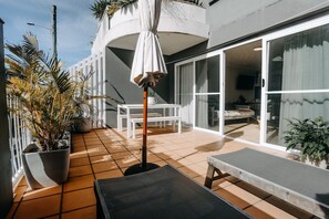 A sunlit patio with a table and chairs, a potted plant, and a sliding glass door leading to a bedroom. - Ohana - The Heart of Byron - Free underground Parking ! (Byron Bay)