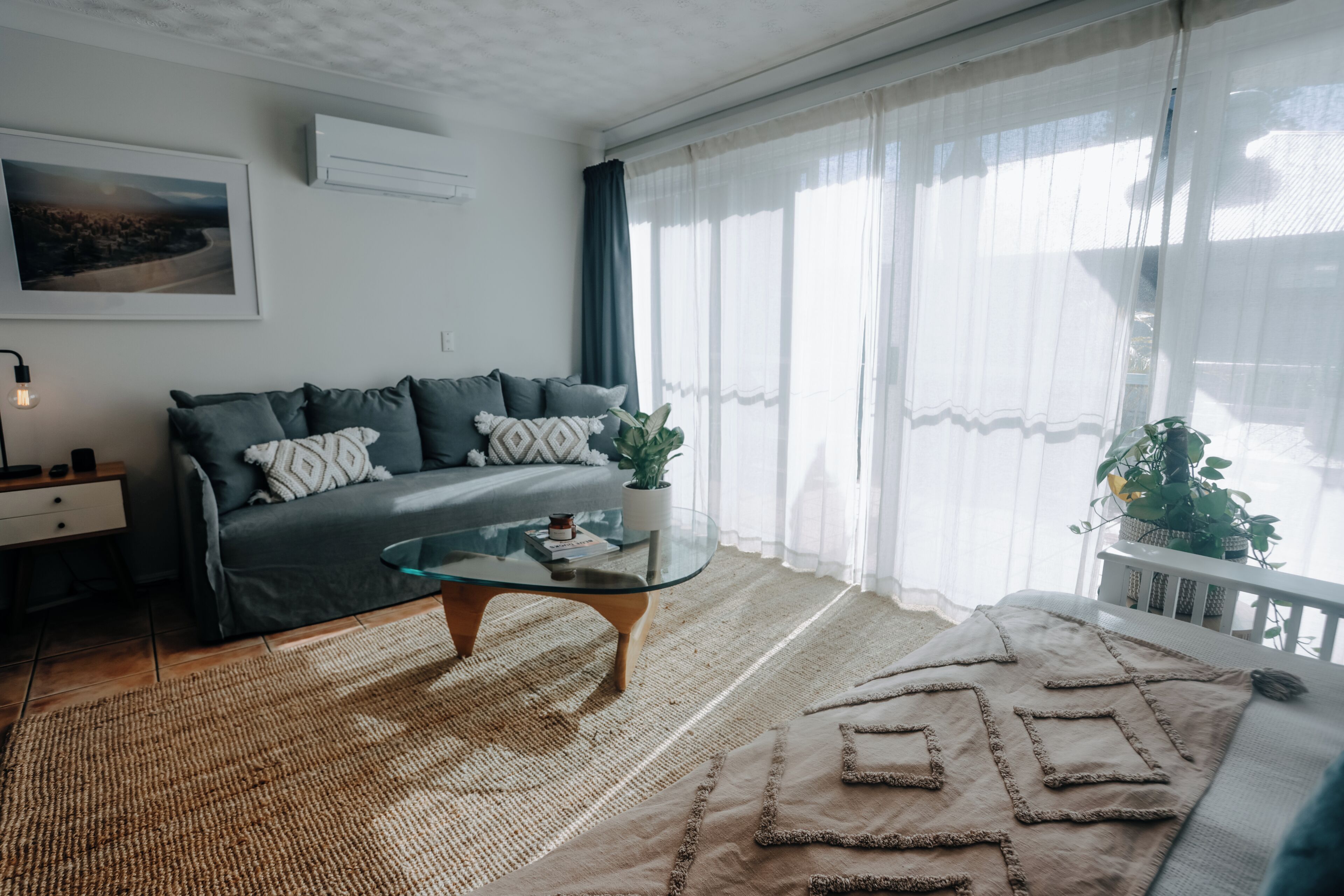 Una sala de estar moderna con un sofá, una mesa de centro de vidrio, una alfombra y una planta en maceta.