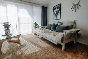 A modern living room with a sofa, a glass coffee table, and a large window with curtains. - Ohana - The Heart of Byron - Free underground Parking ! (Byron Bay)