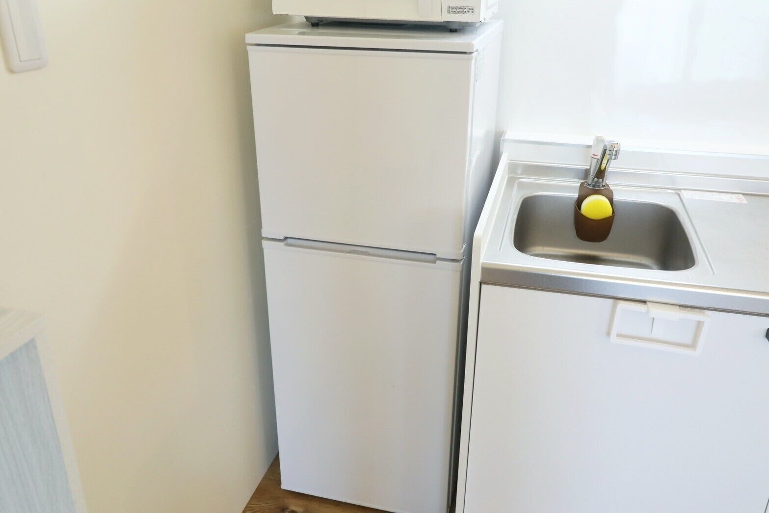 Eine kleine Küche mit einem weißen Kühlschrank, einem Spülbecken mit Armatur und einer Arbeitsplatte.