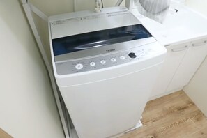 A compact, white Haier washing machine with a digital display and control panel, situated in a small laundry room with wooden flooring.