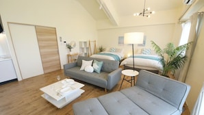 Un soggiorno moderno con un divano grigio, un tavolino bianco e un letto con lenzuola blu.