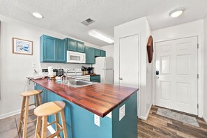 A kitchen with teal cabinets, a white microwave, and a wooden island with stools. - Romar Beach 108 Blue Tides (Orange Beach)