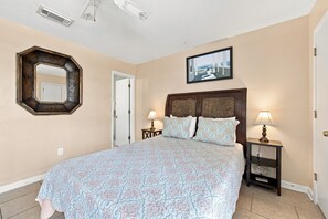 A bedroom with a large bed, two bedside tables with lamps, a mirror, and a framed picture on the wall. - Romar Beach 108 Blue Tides (Orange Beach)