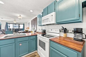 A kitchen with teal cabinets, a white microwave, a stove, and a coffee maker. - Romar Beach 108 Blue Tides (Orange Beach)