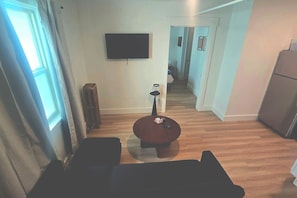 Uma sala de estar com televisão de tela plana na parede, uma mesa de centro redonda e um sofá.