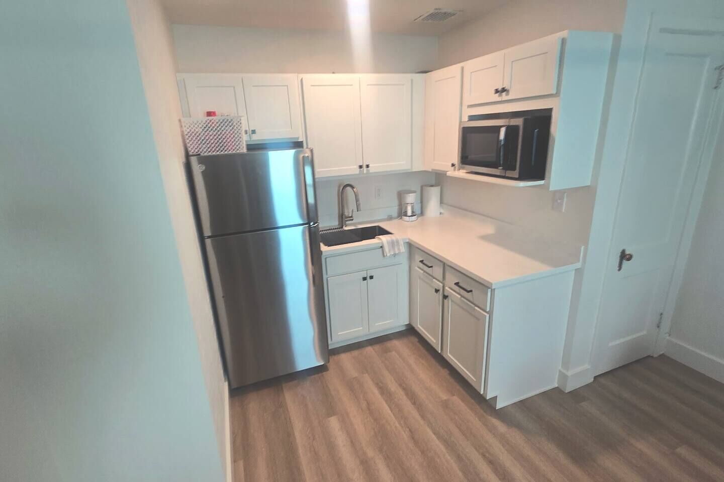 A compact kitchen with white cabinetry, a stainless steel refrigerator, a microwave, and a coffee maker.