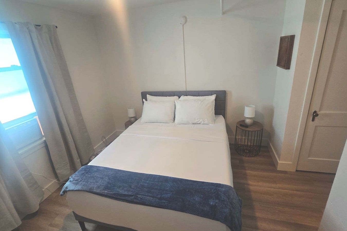 Ein Schlafzimmer mit einem Bett, Nachttischen, einem Fenster mit Vorhängen und einer Tür.