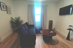 Una sala de estar con un sofá, una mesa de centro, un televisor y una planta.