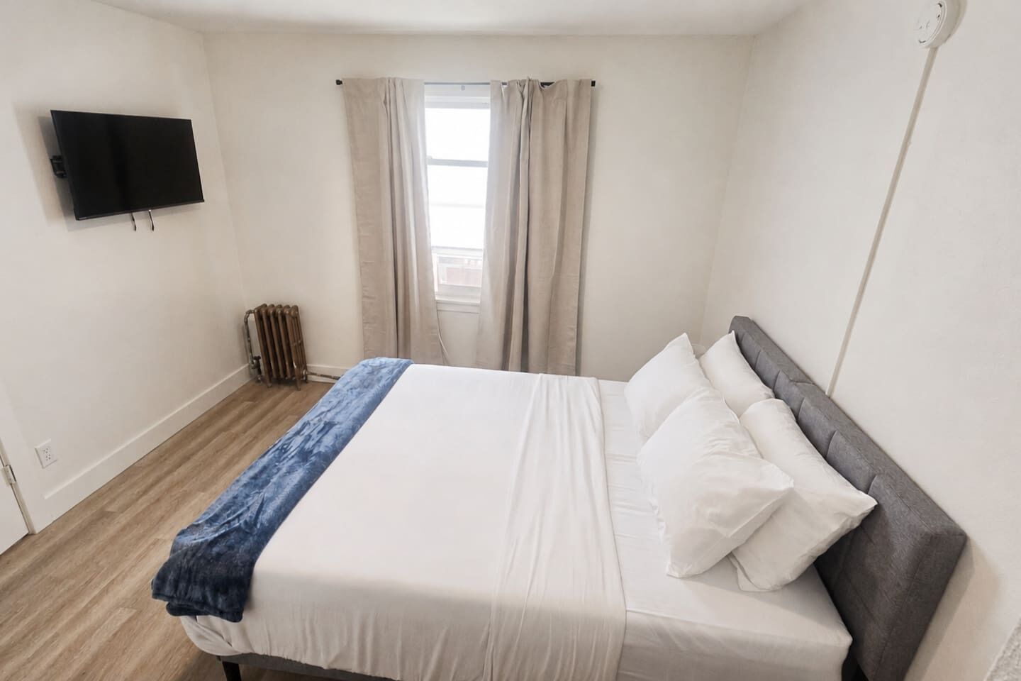 A bedroom with a bed, a television mounted on the wall, and a window with curtains.
