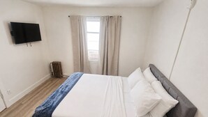 Ett sovrum med en säng, en tv som är monterad på väggen och ett fönster med gardiner.