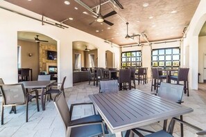 Un amplio espacio al aire libre con mesas y sillas, un ventilador de techo y vistas al exterior.
