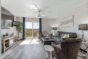 Ein modernes Wohnzimmer mit Sofa, Sessel, Couchtisch und Deckenventilator.