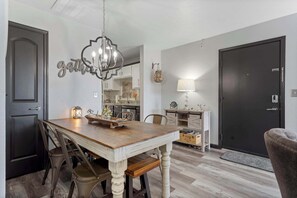 Ein Essbereich mit Holztisch, Stühlen, einer Pendelleuchte und einer Küche im Hintergrund.