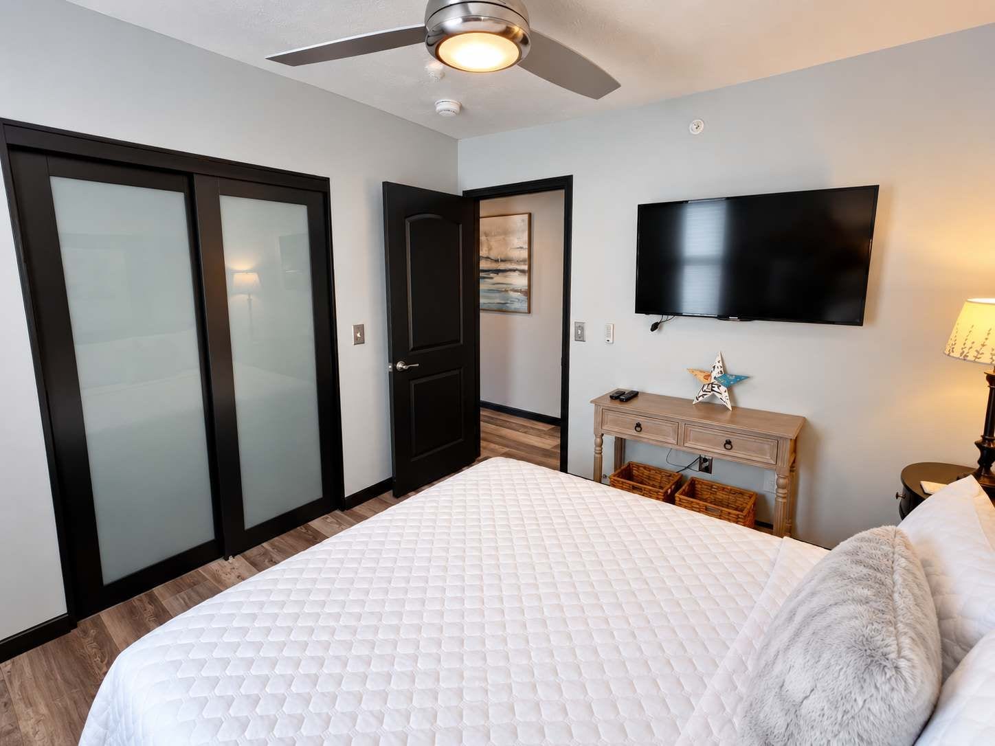 A bedroom with a bed, a television, a desk, and a ceiling fan.
