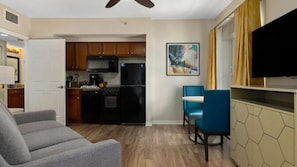 A compact living space with a kitchenette, a dining area with two chairs, a sofa, and a flat-screen TV mounted on the wall. - Cozy, Fun & Exciting resort to stay at ! (Kissimmee)