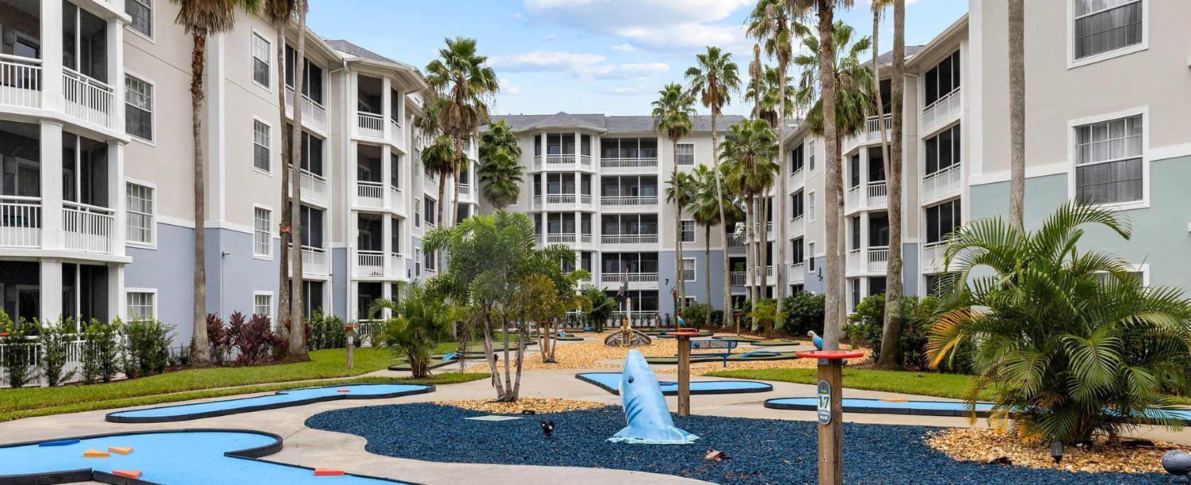 Un hotel de varios pisos con balcones, palmeras y una fuente central.