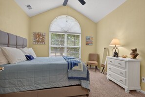 Ein Schlafzimmer mit Bett, Kommode, Stuhl und einem Fenster mit Jalousien.