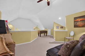Ein Zimmer mit schrägem Dach, einem Schreibtisch, einem Stuhl, einer Couch und einem Gemälde an der Wand.
