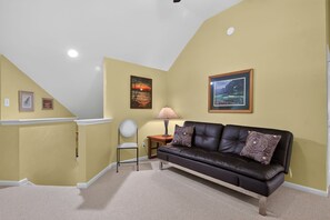 Ein Wohnzimmer mit einem schwarzen Ledersofa, einer Lampe und zwei gerahmten Bildern an der Wand.