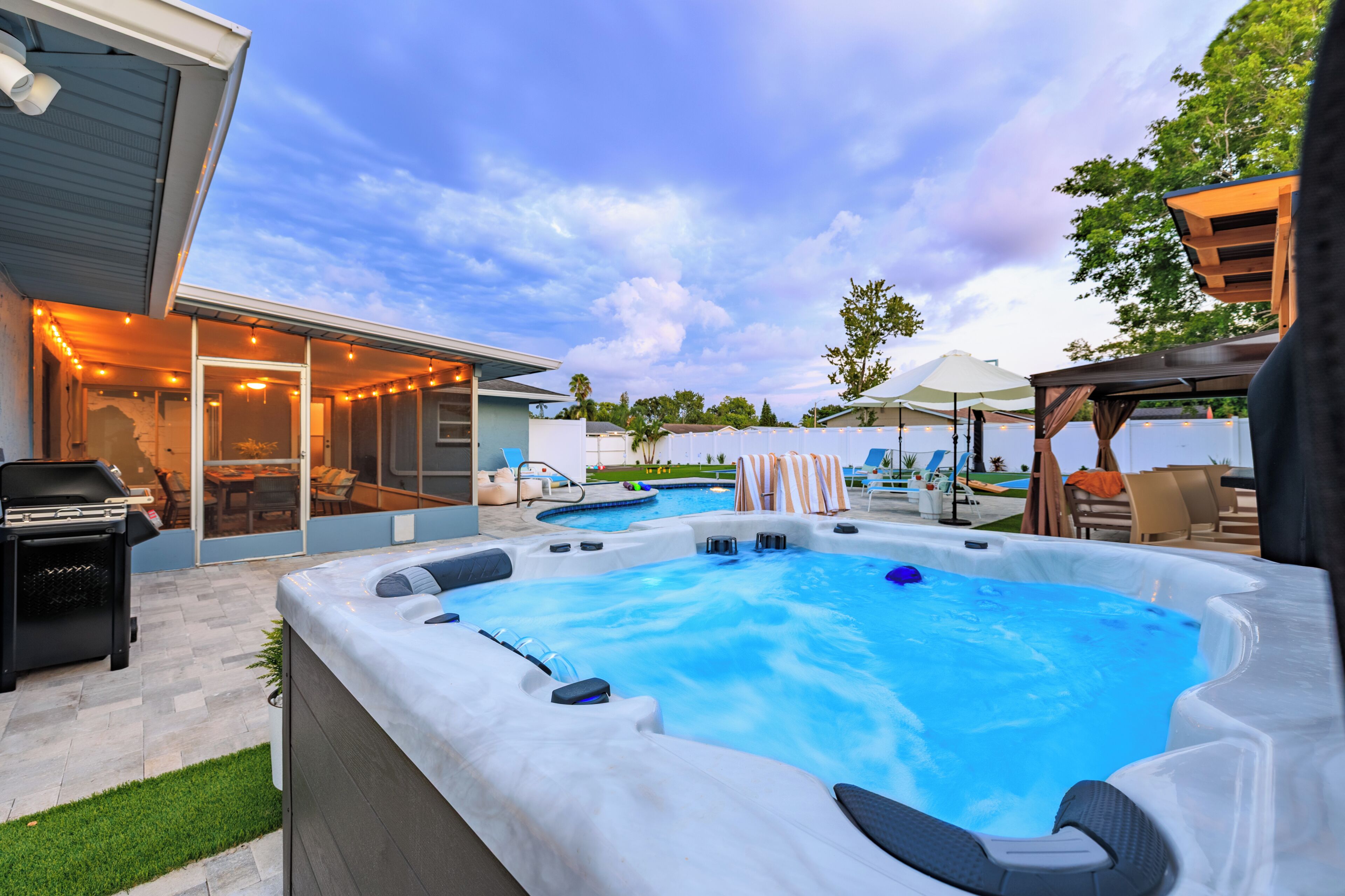 Un patio trasero con un jacuzzi, una piscina y mobiliario exterior.