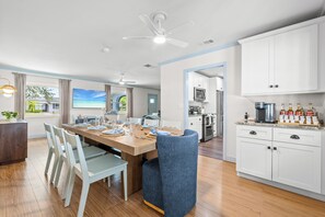 A modern kitchen with white cabinets, a dining area with a wooden table set for four, and a view of the outdoors through large windows. - Full Gym ● 7min to IMG / 16min to AMI ● Sauna & Cold Plunge ● Sport Court ● Pool (Bradenton)