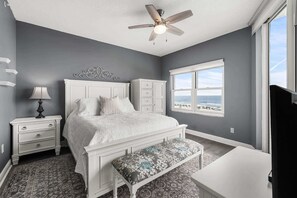 Een slaapkamer met een bed, nachtkastje, dressoir en uitzicht op het strand.