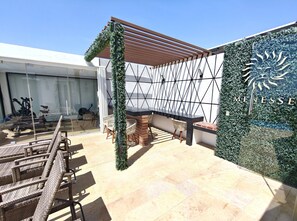 A rooftop patio with a seating area, a pergola, and a wall with a logo. - Paralia Studio by WQR - Pool, Beach, 5th Avenue (Playa del Carmen)