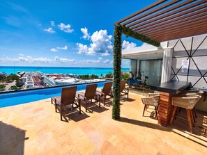 Un espace aménagé au bord de la piscine, offrant une vue sur l’océan et un port de plaisance.