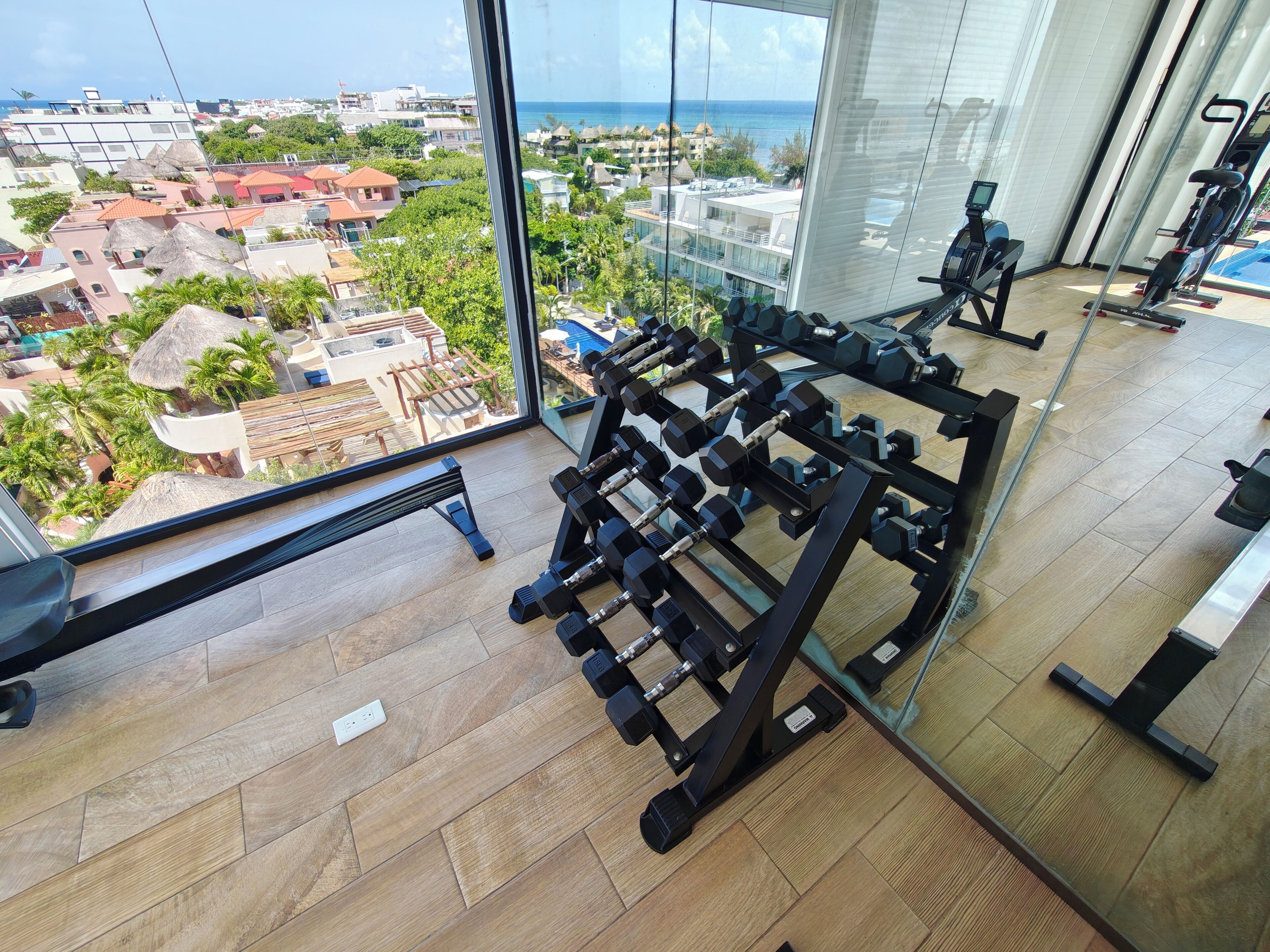 Ein Fitnessstudio mit Trainingsgeräten und Blick auf eine Küstenstadt.