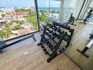 A gym with exercise equipment and a view of a coastal town. - Paralia Studio by WQR - Pool, Beach, 5th Avenue (Playa del Carmen)