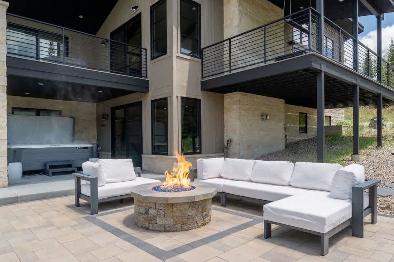 A modern outdoor living area with a stone fire pit, white outdoor furniture, and a two-story building with balconies.