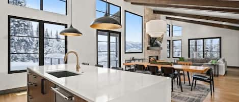 A spacious kitchen with a large island, multiple windows, and a dining area with a view of snow-covered mountains.