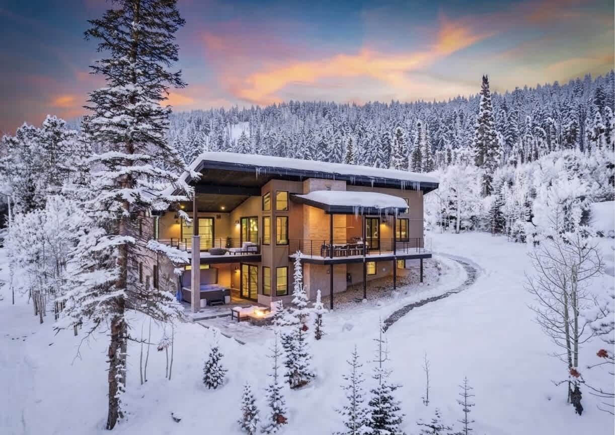 Une cabane en rondins moderne, dotée d’une véranda qui fait le tour de la maison, et entourée d’une forêt enneigée.