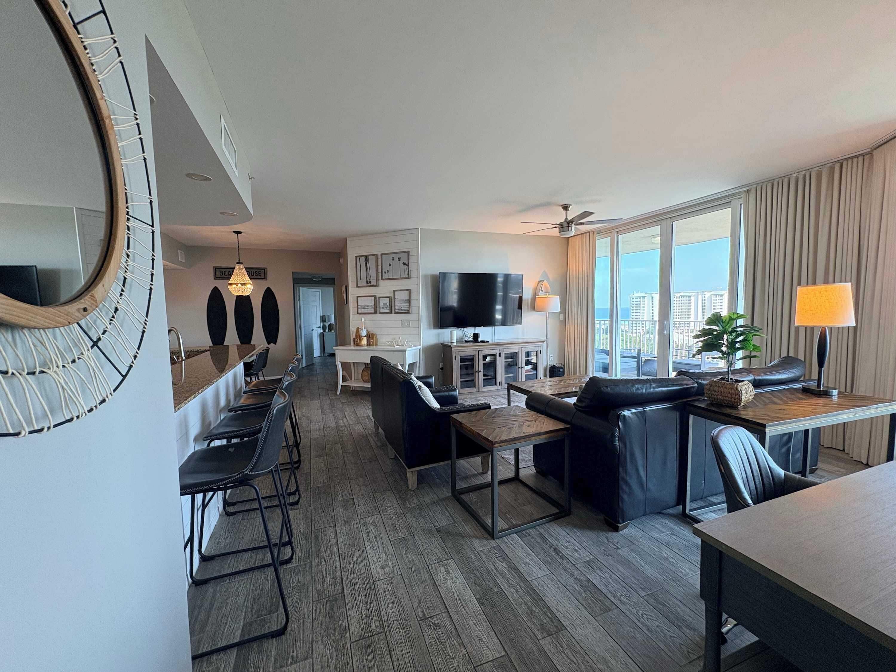 A modern hotel room with a dining area, a living room with a sofa and a TV, and a balcony with curtains.