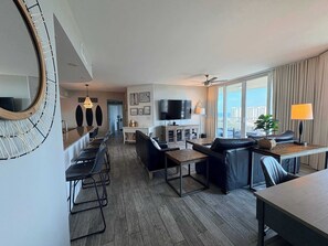 A modern hotel room with a dining area, a living room with a sofa and a TV, and a balcony with curtains. - Coastal Condo with Shared Pools! (Destin)