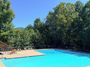 A swimming pool surrounded by trees with lounge chairs and a covered area. - New! Mtn Views with Hot Tub and Fireplace, Fire Pit, Game Room & Work Desk. (Ellijay)