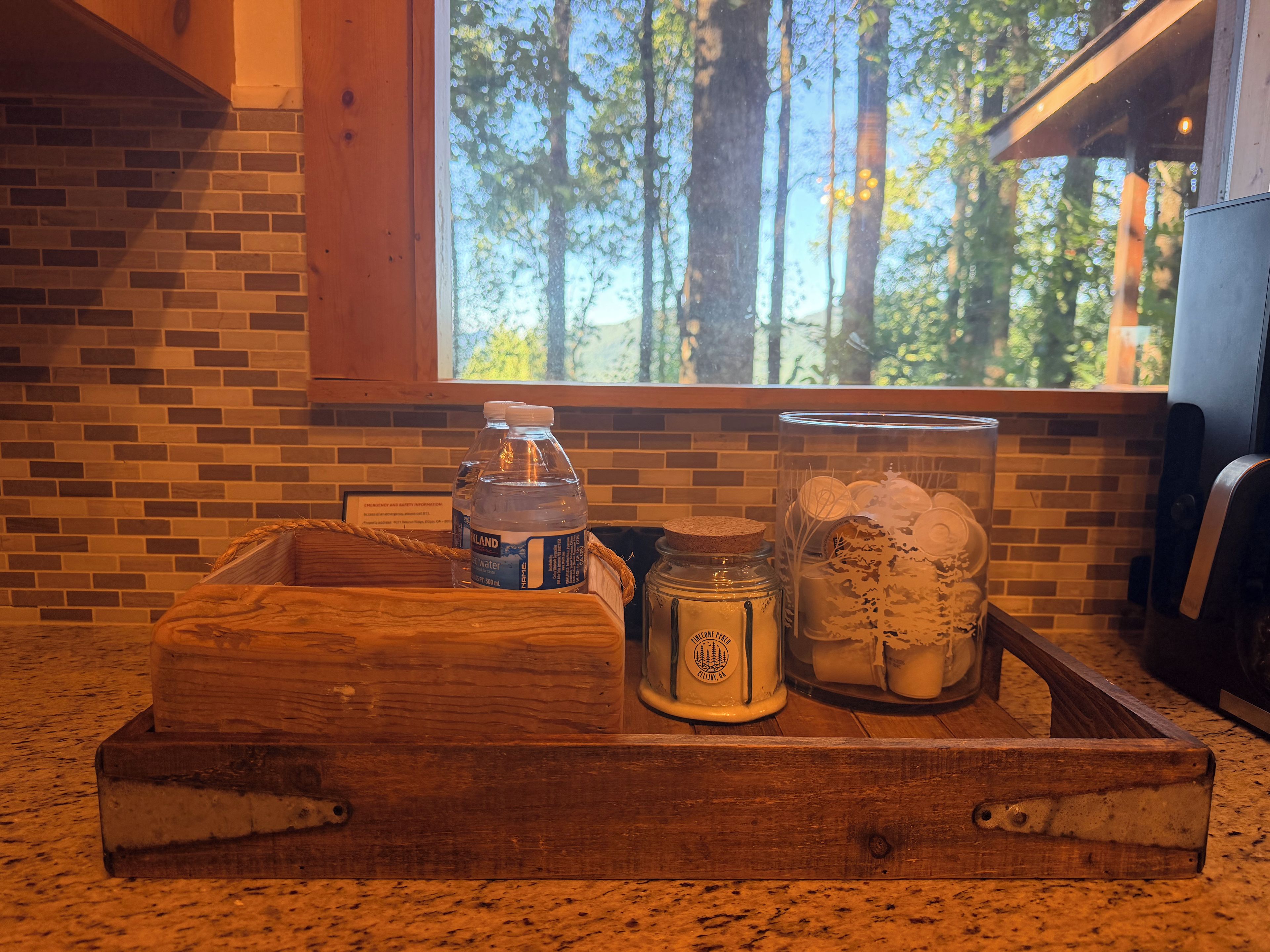 Ein Holztablett mit einer Wasserflasche, einem Einmachglas und einem Glasbehälter auf einer Küchenarbeitsplatte.