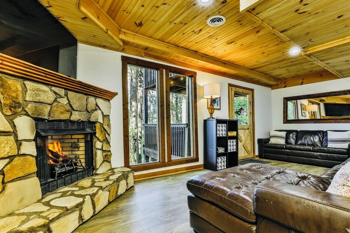 Una sala de estar acogedora con chimenea de piedra, un sofá de cuero y una estantería.