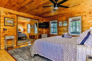 A wooden cabin interior with a bed, a television, and a ceiling fan. - New! Mtn Views with Hot Tub and Fireplace, Fire Pit, Game Room & Work Desk. (Ellijay)