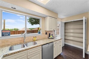 A kitchen with a granite countertop, white cabinets, a double sink, and a window with a view of greenery. - 6BR Dallas Getaway - Next to Green Trails & Joe Pool Lake (Dallas)