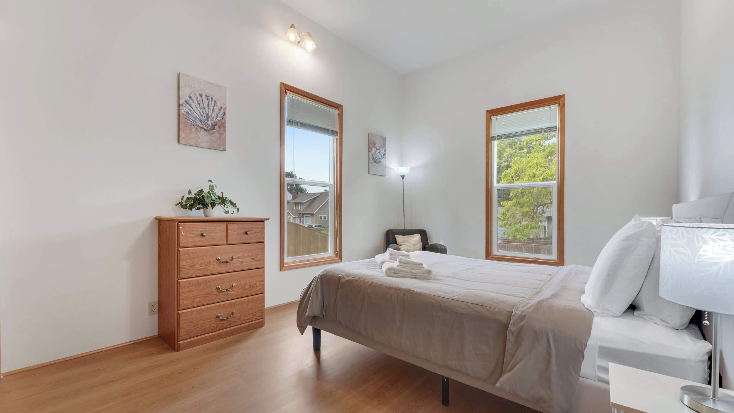 A bedroom with a bed, a dresser, two windows, and a lamp.