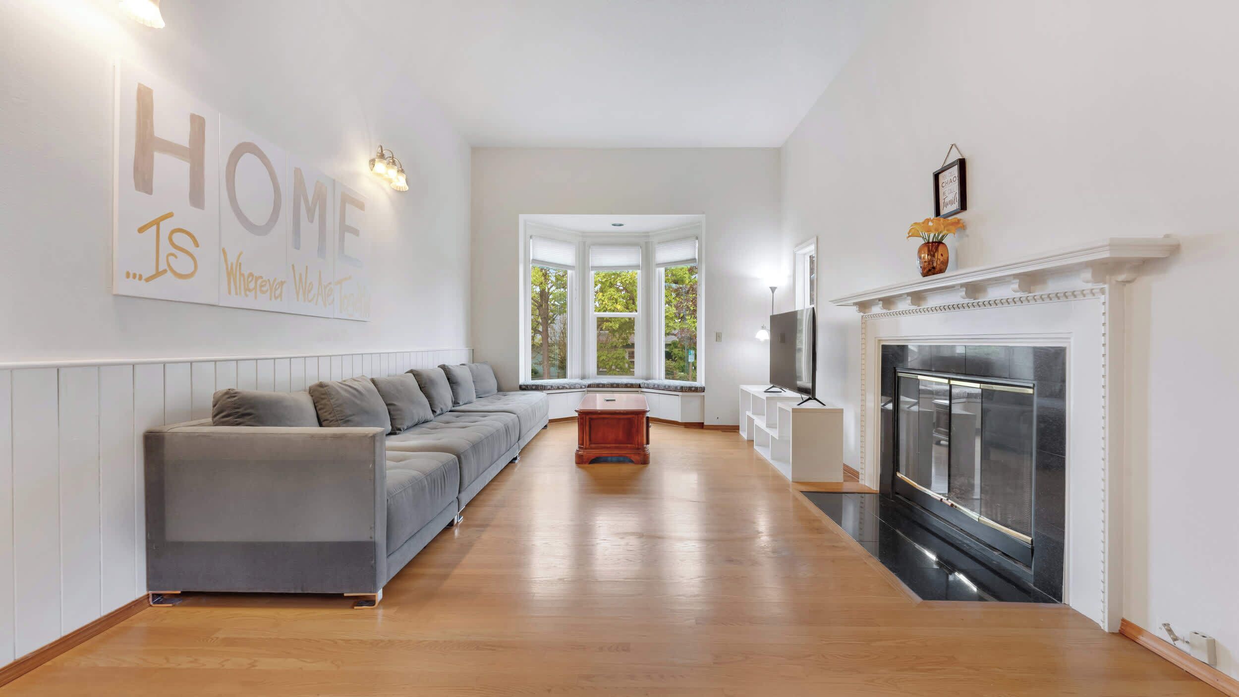 A modern living room with a grey sofa, a fireplace, and a large window.