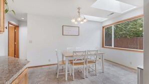 A kitchen with a dining table, chairs, a pendant light, a window, and a framed quote on the wall.