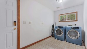 A laundry room with two blue washing machines, a vacuum cleaner, and a door with a golden handle. - Walk-to-UO Retreat with Private Patio (Eugene)