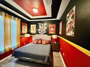 Een slaapkamer met een bed, een nachtkastje, een lamp en Mickey Mouse posters aan de muur.