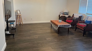 Uma sala de estar espaçosa com piso de madeira, uma mesa de jantar com toalha de renda e um sofá com almofadas estampadas.