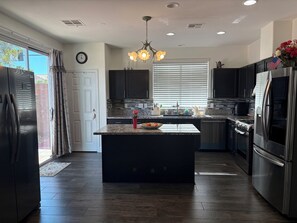 Una cocina moderna con muebles oscuros, una isla central, electrodomésticos de acero inoxidable y un ventanal con persianas.