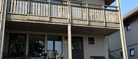 A two-story building with a balcony, outdoor seating, and a door.