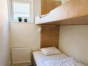 Habitación con literas, ventana, radiador y una pequeña planta en maceta.
